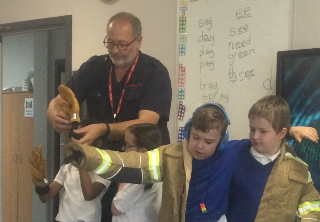 Four young students are seen trying on Fireman's uniform, under the supervision of a Fire Service staff member.