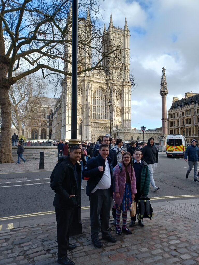Five students are pictured posing for the camera, alongside their teachers, outside Westminster Abbey during a trip to London to attend the annual Commonwealth Day service.