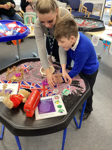 A female staff member is seen assisting a pupil in creating some union flags to be used to celebrate King Charles III's Coronation.
