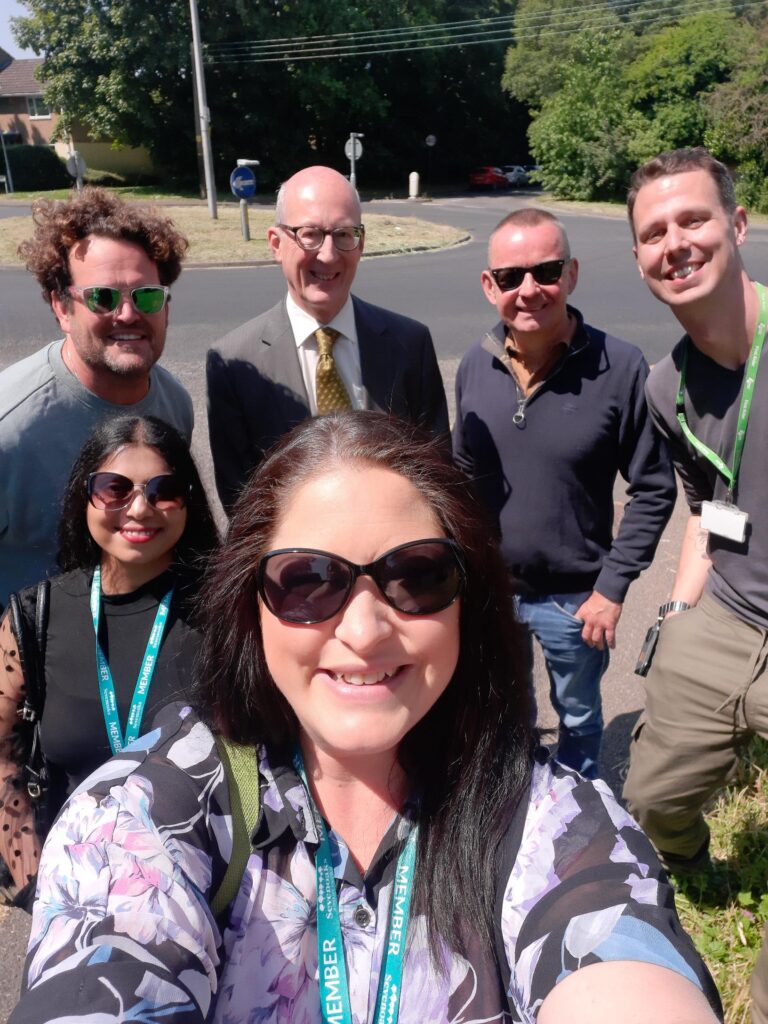 Six members of staff are pictured taking a group selfie photo together, whilst outdoors on a trip to an event.