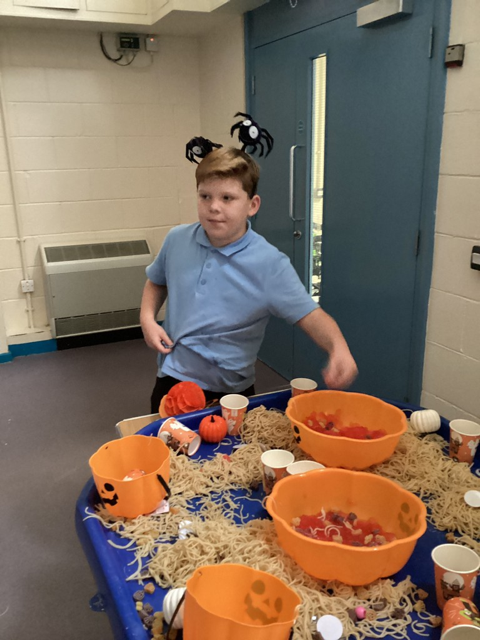 A young male student from Phase 2 is pictured standing alongside a table, full of bowls of sweets for Halloween.