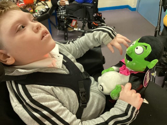A young boy is seen sat in a wheelchair and holding a soft toy of the character 'Count Dracula' in his hands.