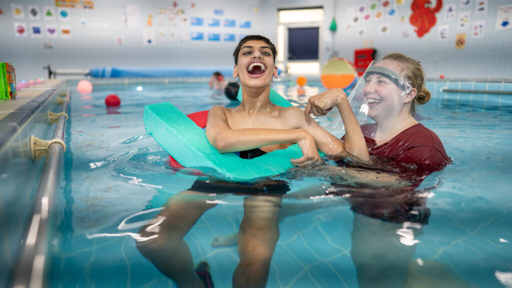 A boy in swimming pool with a teacher, smiling and laughing