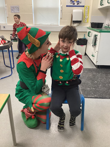 A member of staff is seen laughing with a young boy in the kitchen area. They are both dressed up as Santa's elves.