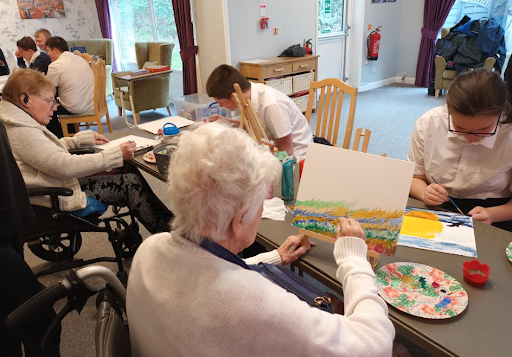 Two elderly residents at a care home are pictured working with crafts to create some artwork, together with Milestone Academy students.