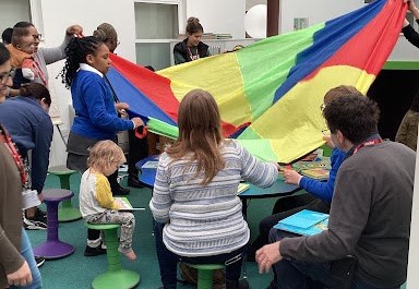 Students, staff and parents are pictured participating in a fun activity together, using a parachute, during a Reading Brunch session.