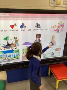 A young girl is pictured pointing at something on an Interactive Board at the front of the classroom.
