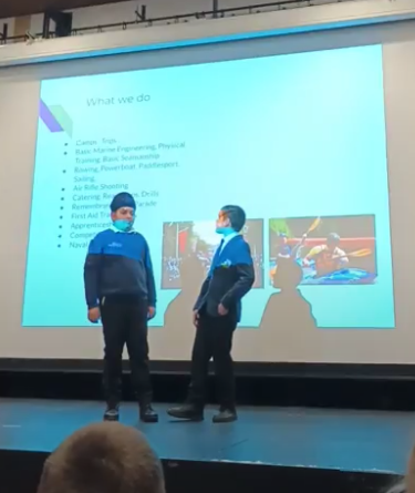 Two student cadets are pictured standing onstage delivering a presentation to some M@L students in the audience.