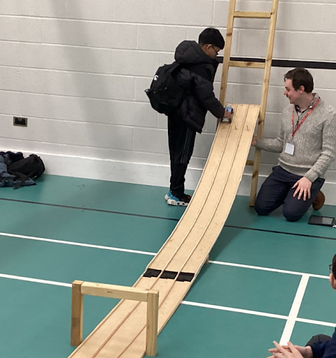 A student and a teacher watching the student's project vehicle rolling down a ramp